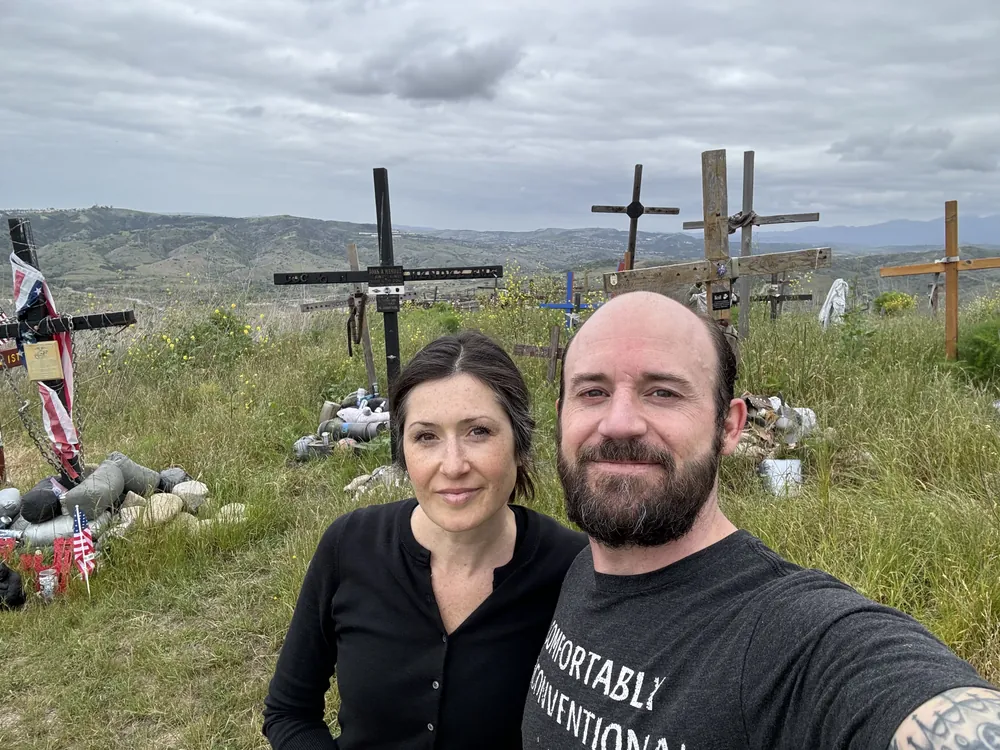 Sonny and a woman standing before a hillside of memorial crosses and US flags