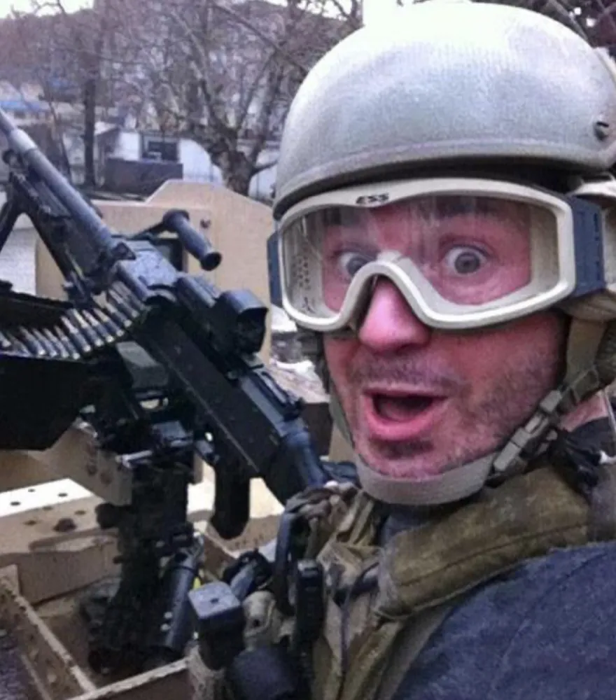 Sonny in goggles and helmet making a goofy face behind a machine gun
